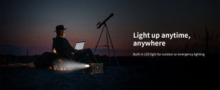 Person with laptop and telescope at night, illuminated 